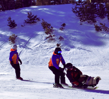 This is an image of someone being pushed in adaptive ski equipment