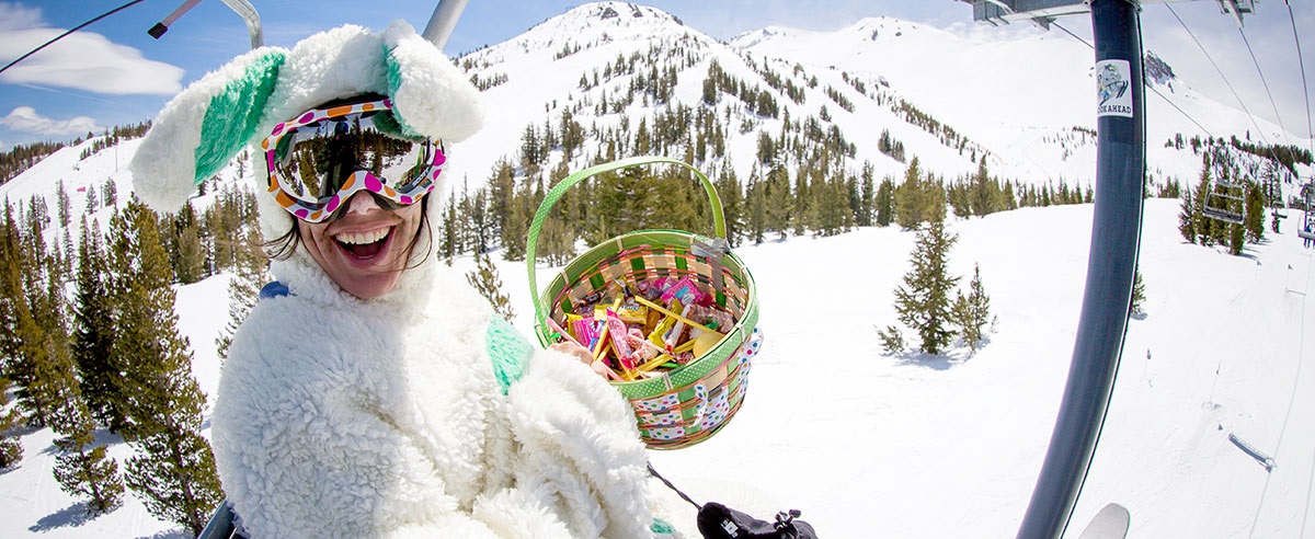 This is a picture of a woman dressed as the easter bunny riding on one of the chair lifts on the mountain, holding a basket full of candy.